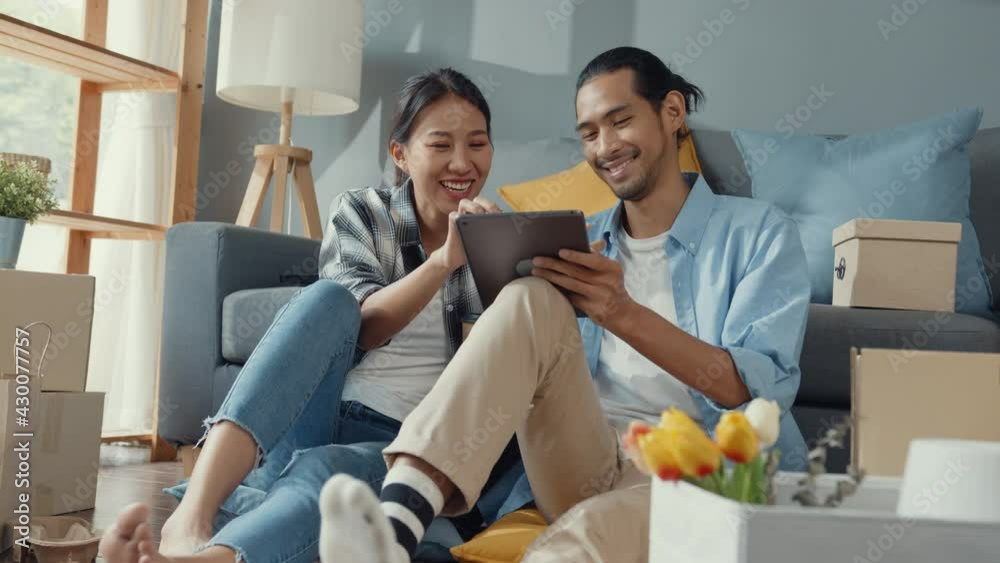 Happy asian young attractive couple man and woman use tablet online shopping furniture decorate house with carton package move in new house. Young married asian moving home shopper online concept.