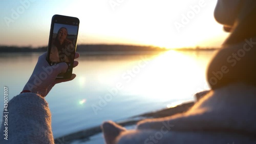A young girl in nature takes a selfie on her phone at sunset