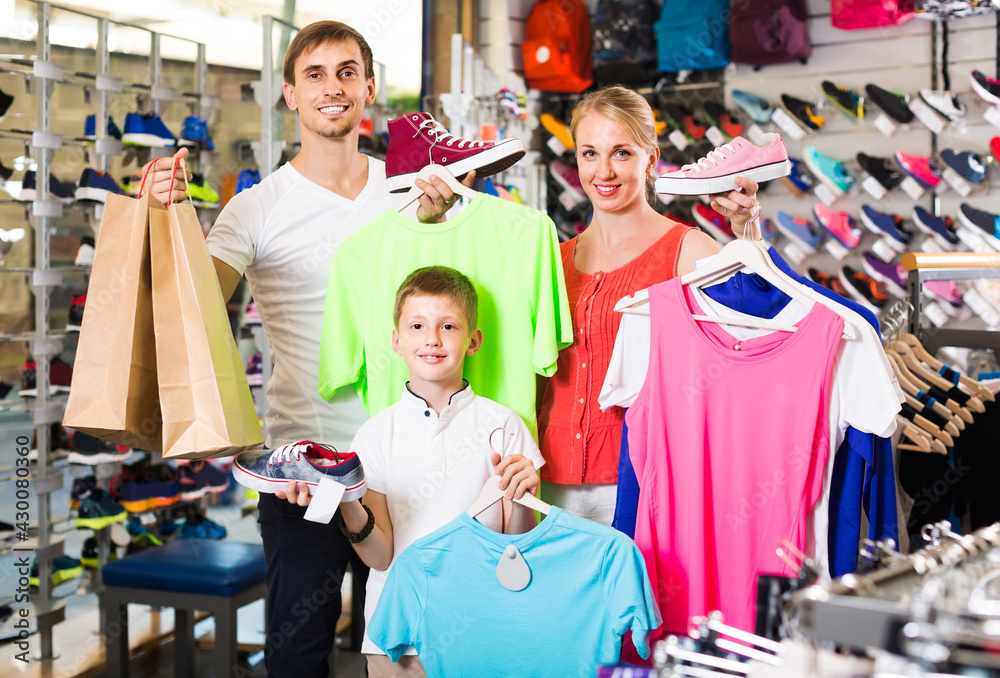Fototapeta premium positive spanish couple with boy choosing shoes in sport shop