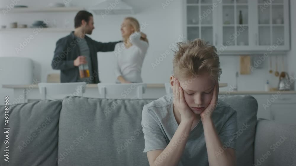 Unhappy little boy sitting alone on sofa and listening his arguing parents, drunk man quarreling with his wife Unhappy little boy sitting alone on sofa and listening his arguing parents, drunk man quarreling with his wife