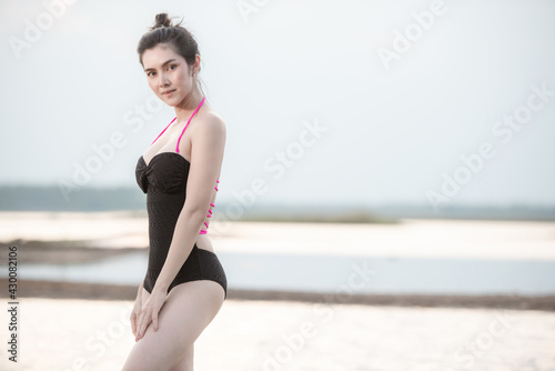 Portrait Beautiful woman in swimwear with a one-piece swimsuit beautiful sports body walking and posing on a beach © Chanwit