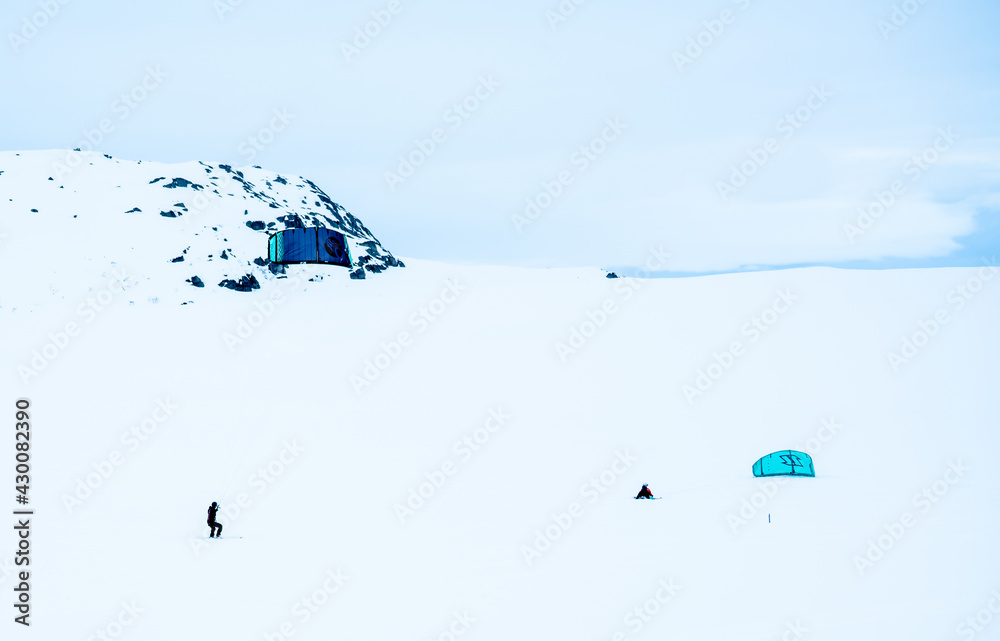 People Snowkiting on a frozen snowy mountain plain on a cold winters day.