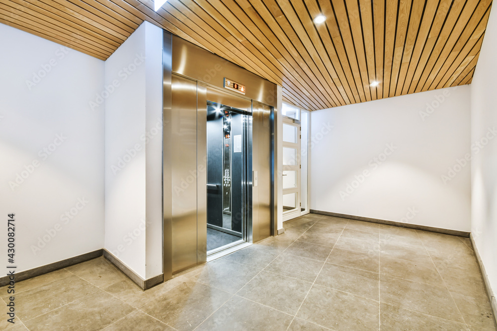 Shiny elevator with opened door located in illuminated hall of contemporary apartment building with tiled floor - obrazy, fototapety, plakaty 