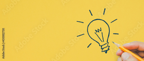 Hand holding pencil drawing light bulb yellow background, Creative idea, innovation and inspiration concept, copy space photo