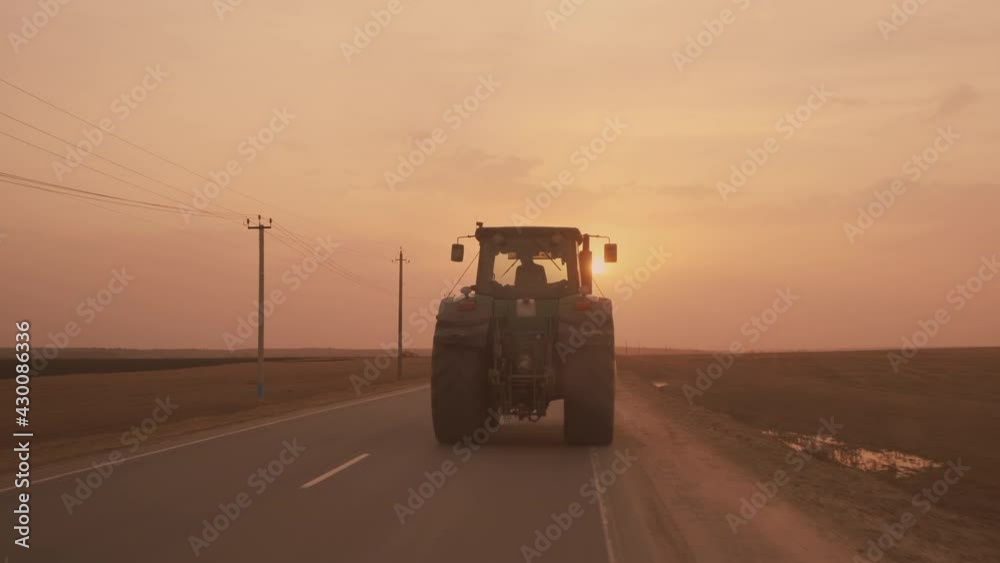 Farm tractor with large wheels driving on country road at sunset after sowing or harvesting in field. Farm tractor with large wheels driving on country road at sunset after sowing or harvesting in field.