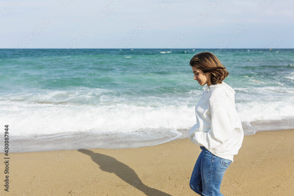 Young relaxed woman enjoying and walking alone on the beach - Copy space on the left side Young relaxed woman enjoying and walking alone on the beach - Copy space on the left side