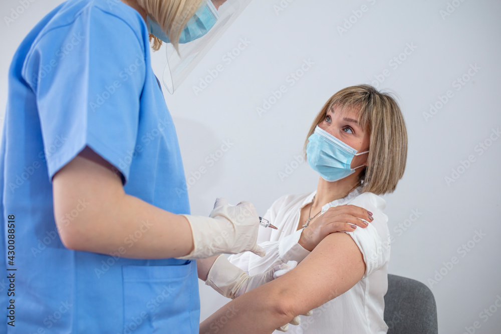Doctor's hands in surgical gloves preparing COVID-19 vaccine for female patient. Vaccination, immunization campaign, disease prevention concept. Professional nurse giving flu injection to patient