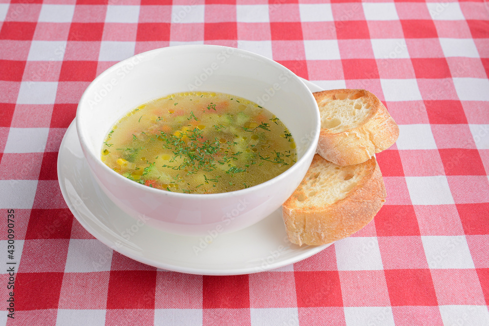 Chicken broth soup with vegetables served in a white bowl over red plaid tablecloth. Ukrainian cuisine concept. Chicken broth soup with vegetables served in a white bowl over red plaid tablecloth. Ukrainian cuisine concept.