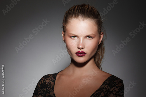 Beautiful blonde girl with hair gathered in a ponytail with burgundy lips on dark grey background. photo