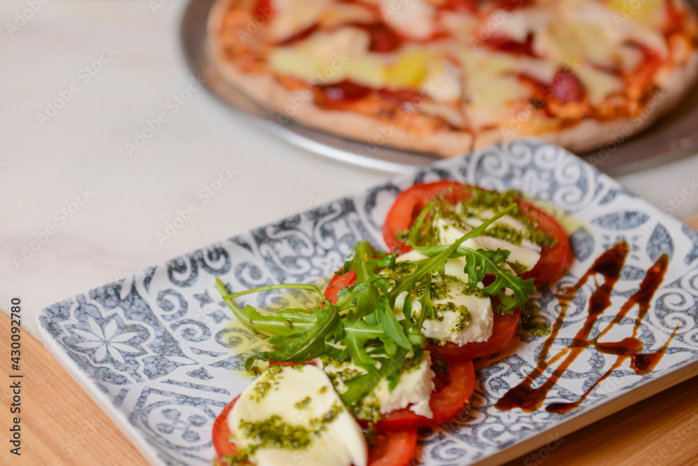 Classic caprese salad on table with pizza. Photo with blurred background. Traditional Italian cuisine concept.