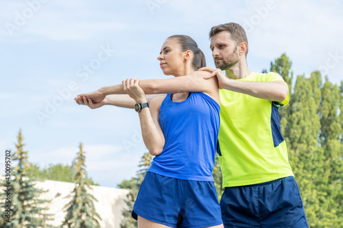 Man helps a woman during sports stretching. Warm up before training with a trainer.
