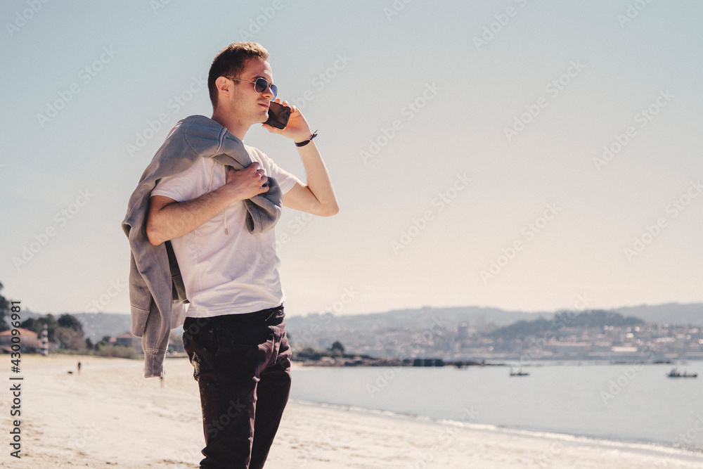 young man walking on the beach talking on the mobile phone young man walking on the beach talking on the mobile phone