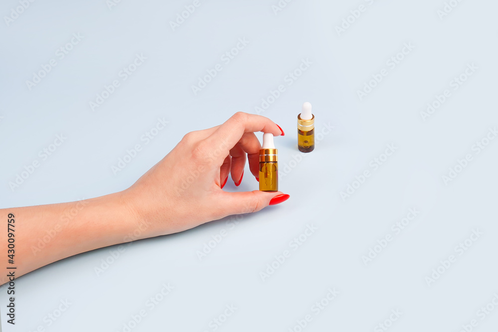 Beautiful young woman's hand and bottles of hyaluronic acid with pipette on blue table, copy space. Beautiful young woman's hand and bottles of hyaluronic acid with pipette on blue table, copy space.