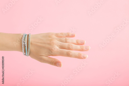 Bracelet of small gems on young adult woman wrist isolated on light pink background. Pastel color. Beautiful groomed hand. Closeup. Side view.