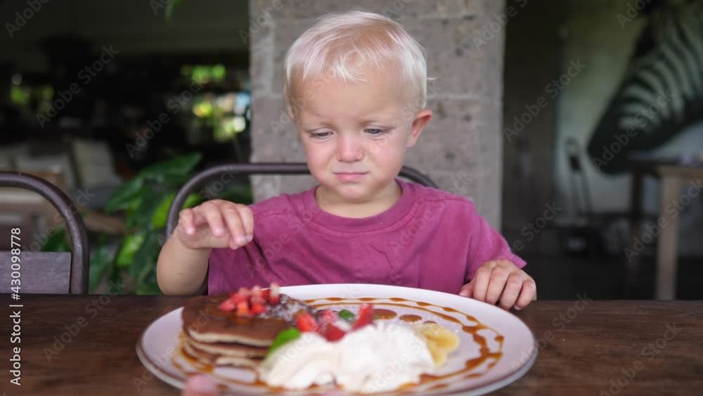Cute little tired caucasian baby does not want to eat pancakes with fruits and cream Cute little tired caucasian baby does not want to eat pancakes with fruits and cream