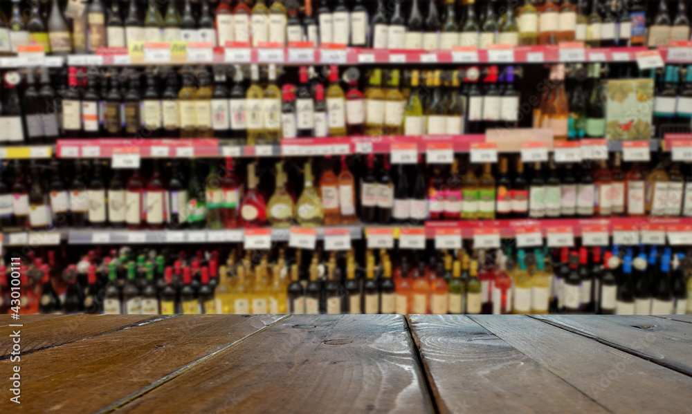 Blurred image of a liquor store with drinks. Wine bottles on the shelves. In the foreground is a table or counter.