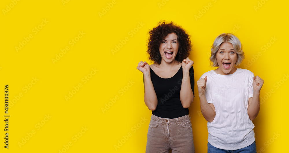Curly haired friends are shocked by something posing on a yellow studio wall Curly haired friends are shocked by something posing on a yellow studio wall