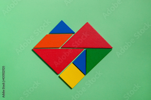 Heart of colorful tangrams in green background 