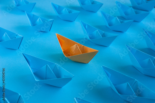 Origami in blue and orange on a blue paper background. An orange paper boat among many blue ones. Teamwork concept. Concept to stand out from the crowd.