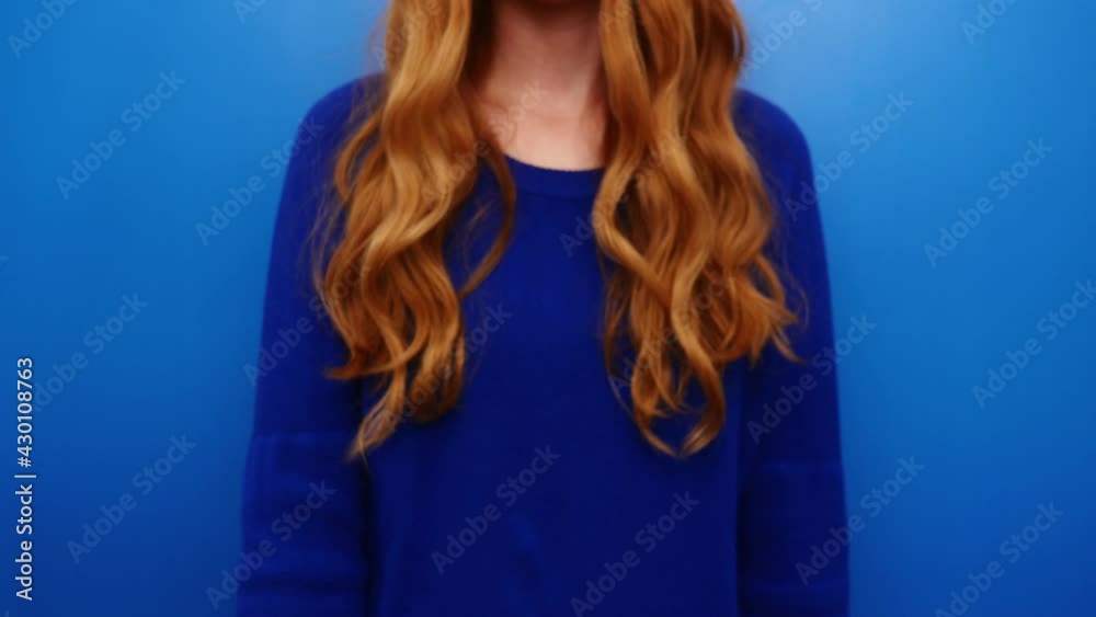 Beautiful ginger redhead young girl wearing blue sweater posing isolated on blue color background in studio. Beauty makeup concept. Showing playing with brush