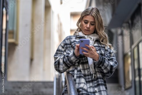 Pretty Caucasian young woman with coat and smartphone in hand