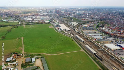 4K aerial footage moving sideways on the edge of a town. Urban and rural. Train lines and industrial areas border green fields and countryside in Reading, Berkshire, UK