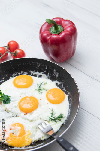 Scrambled eggs in frying pan bell pepper, cherry tomato on the background of a light wooden table. National Ukrainian or belorussian food. Breakfast, lunch. Top view, selective focus, rustic style. photo