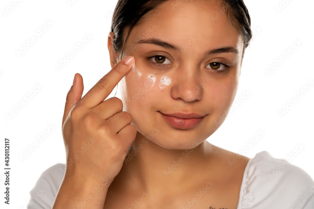 a young woman applies face cream under her eyes a young woman applies face cream under her eyes