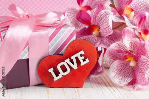 Valentines Day background with giftbox, pink orchid flower and heart with word love on white wooden surface