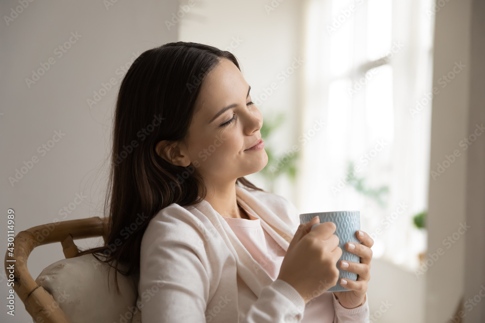 Happy woman enjoying fresh aroma of coffee or tea, holding cup. Peaceful satisfied girl drinking hot morning beverage, spending leisure time at home, smiling with closed eyes. Relaxation concept Happy woman enjoying fresh aroma of coffee or tea, holding cup. Peaceful satisfied girl drinking hot morning beverage, spending leisure time at home, smiling with closed eyes. Relaxation concept