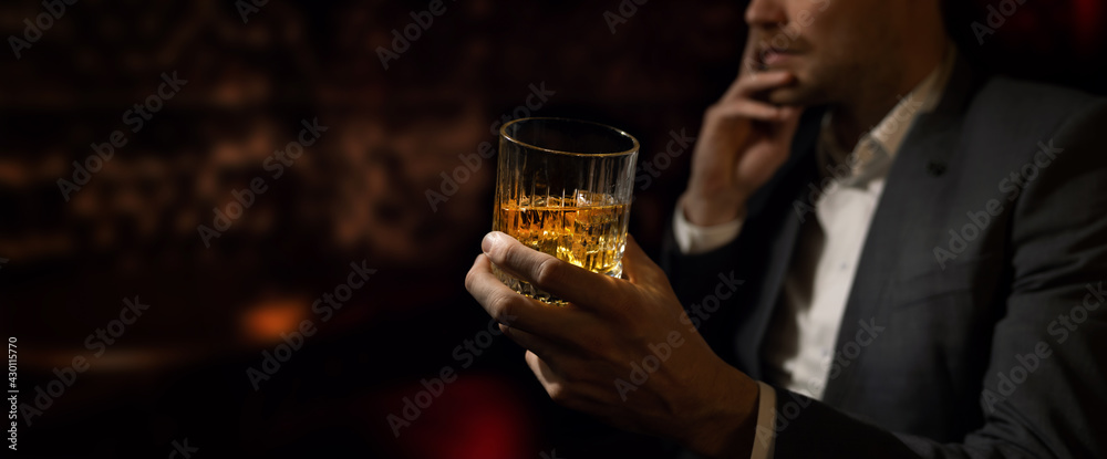 man wearing suit sits in the luxury bar in gentlemen club and drink whiskey. copy space