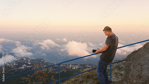 A young man enthusiastically photographs the clouds at his feet. A man stands high in the mountains above the clouds and takes pictures of a beautiful landscape