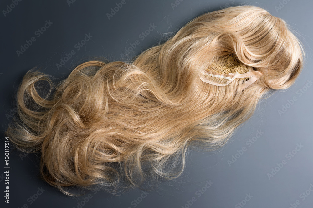 Naklejka premium Female blonde wig close up on grey background. Golden human hair weaves, extensions and wigs. Woman beauty concept.