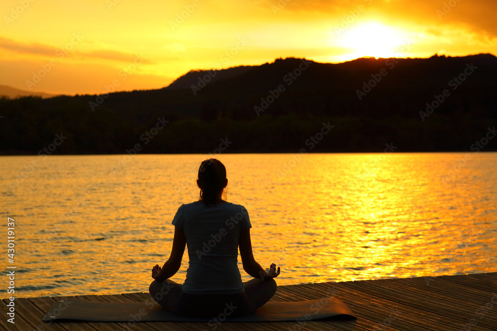 Silhouette of a woman doing yoga at sunset in a lake