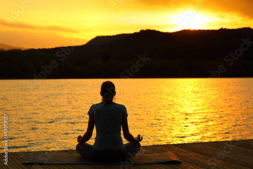 Silhouette of a woman doing yoga at sunset in a lake © PheelingsMedia