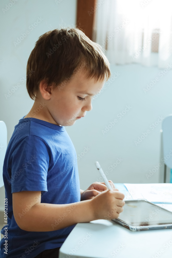 Cute boy in blue t shirt using digital tablet or computer for drawing his picture, using stylus . New technology art, online education Cute boy in blue t shirt using digital tablet or computer for drawing his picture, using stylus . New technology art, online education