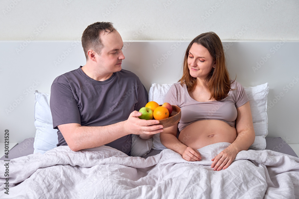 A man gives a pregnant woman a tray with a plate of fruit - the concept of proper nutrition during pregnancy, weight control