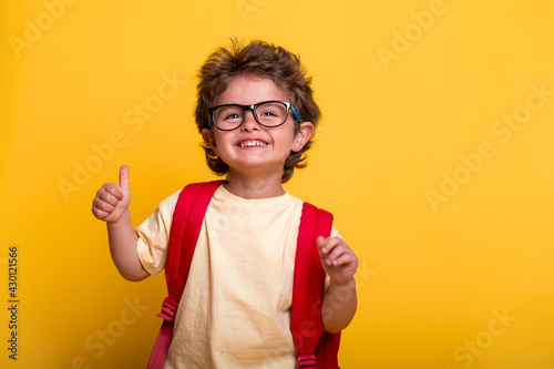 Beautiful little kid boy with backpack isolated on yellow background. Ready to go back to school. education concept. Child in eyeglasses. Happy smiling pupil