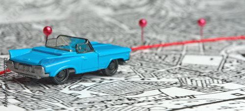 Concept. Following the route. A toy blue convertible is driving across the map. The direction is indicated by red safety pins. Finding a path, a goal, a road.