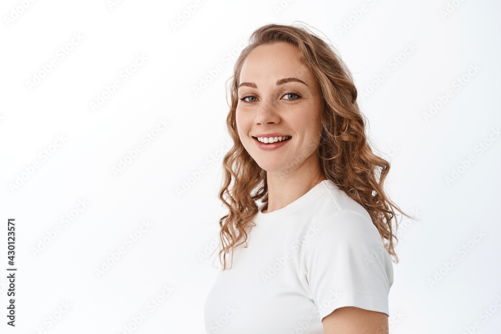 Portrait of attractive blond woman with curly hairdo, turn head at camera and smile happy, looking carefree, standing over white background Portrait of attractive blond woman with curly hairdo, turn head at camera and smile happy, looking carefree, standing over white background