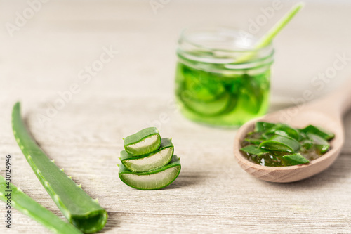 Fresh aloe vera plant, stem slices and gel in glass jar on wooden background, skin therapy, natural organic cosmetic concept.