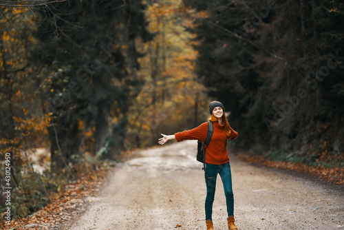 happy woman hiker with backpack walks on the road in autumn forest