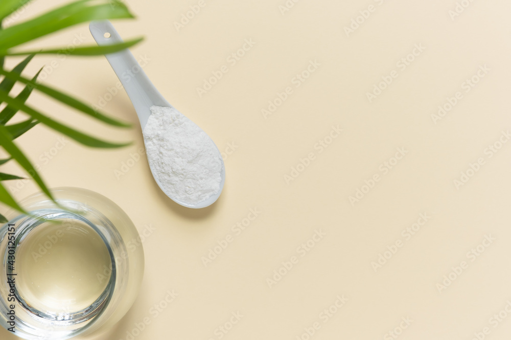 Collagen powder in a spoon and a glass of water on a beige background with a copy space. Extra protein intake