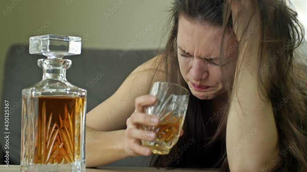 Crying woman drinking alcohol alone. An attempt to relieve stress. Negative emotions, bad mood due to unloved work, personal problems, parting with a lover, cheating. Crying woman drinking alcohol alone. An attempt to relieve stress. Negative emotions, bad mood due to unloved work, personal problems, parting with a lover, cheating.