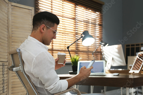 Freelancer with cup of coffee using smartphone while working indoors. Space for text