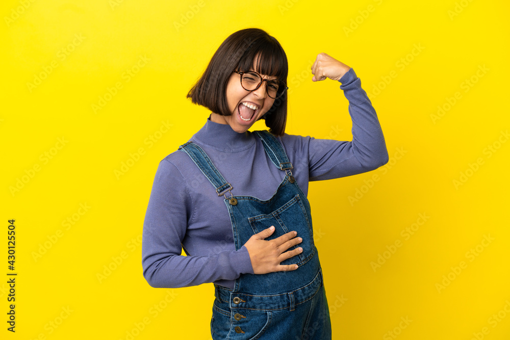 Young pregnant woman over isolated yellow background doing strong gesture Young pregnant woman over isolated yellow background doing strong gesture