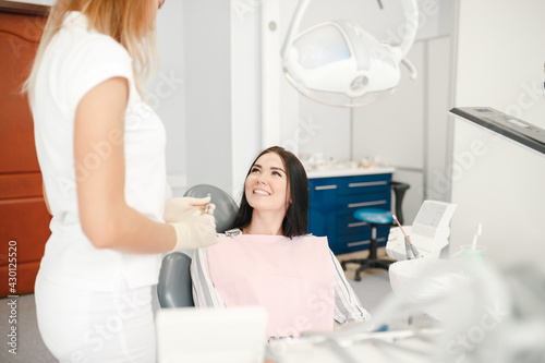 Young woman getting dental treatment. Young female doctor dentist look at female patient in the chair, explaining tretatment plan