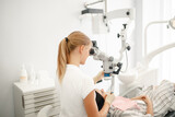 A dentist is looking in a special microscope for dentist in a laboratory wit patient sit in the chair. Close-up of female dentistry at the workplace