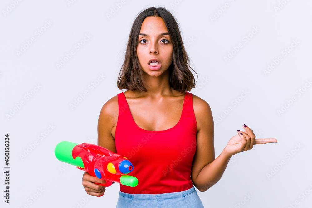 Young mixed race woman holding a water gun isolated pointing to different copy spaces, choosing one of them, showing with finger. Young mixed race woman holding a water gun isolated pointing to different copy spaces, choosing one of them, showing with finger.