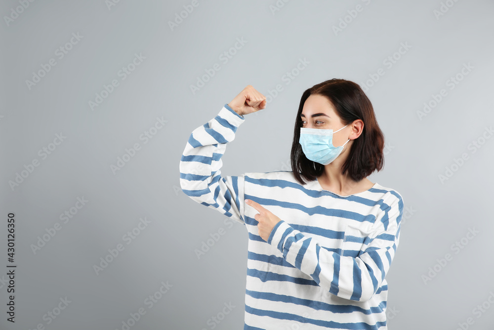 Woman with protective mask showing muscles on light grey background, space for text. Strong immunity concept Woman with protective mask showing muscles on light grey background, space for text. Strong immunity concept